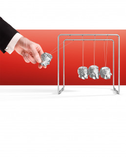 A hand is going to release a ball of a Newton's cradle pendulum. The balls are shaped like human heads.